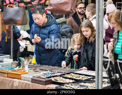 Ein Mann und zwei kleine Mädchen, die einen Juwelierstand auf dem Antiques & Collectables Market in Jubilee Hall, Covent Garden, London, England, Großbritannien, besichtigen Stockfoto