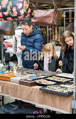 Ein Mann und zwei kleine Mädchen, die einen Juwelierstand auf dem Antiques & Collectables Market in Jubilee Hall, Covent Garden, London, England, Großbritannien, besichtigen Stockfoto