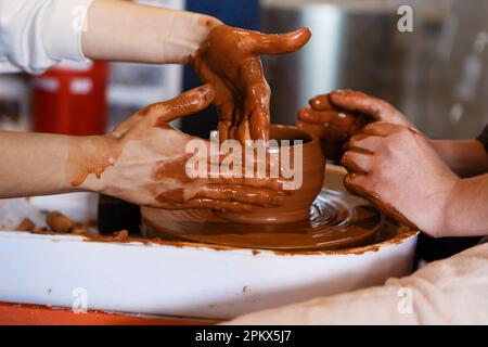 potter mit einem Schüler auf dem Töpferrad macht Teller aus Lehm Stockfoto