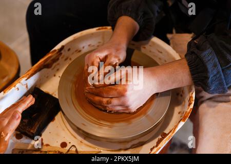 potter mit einem Schüler auf dem Töpferrad macht Teller aus Lehm Stockfoto