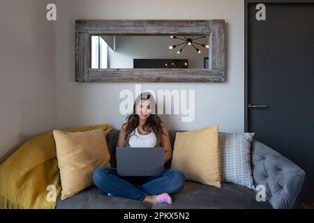 Frau Mit Laptop, Die Zu Hause Auf Dem Sofa Sitzt Stockfoto