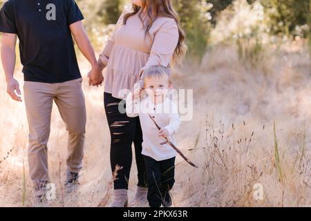 Ein niedliches Kleinkind, das einen Stock trägt, der mom und Dad zieht Stockfoto