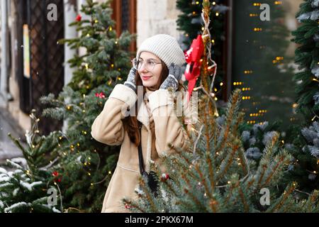 Frau im Winter mitten auf dem weihnachtsmarkt zwischen weihnachtsbäumen Stockfoto