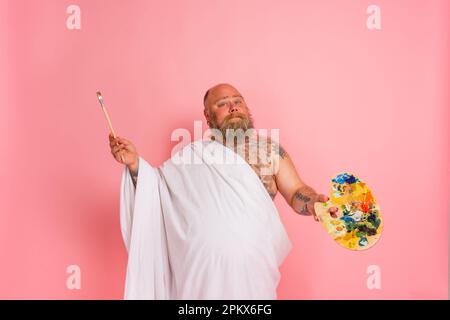 Fat man benimmt sich wie ein wichtiger Künstler mit Pinsel und Farbe in der Hand Stockfoto