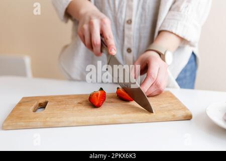 Eine Köchin schneidet rote, frische Erdbeeren mit einem Messer in der Küche Stockfoto