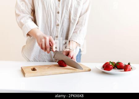 Eine Köchin schneidet rote, frische Erdbeeren mit einem Messer in der Küche Stockfoto