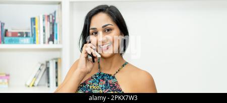 Lachende mexikanische Erwachsene Frau, die zu Hause telefoniert Stockfoto