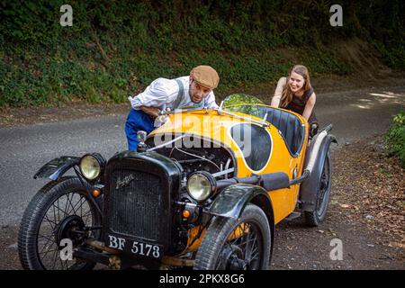 Männer und Frauen schieben auf dem Land den heruntergekommenen Oldtimer auf die Straße.Paar schiebt ihr abgebrochenes Auto. Stockfoto