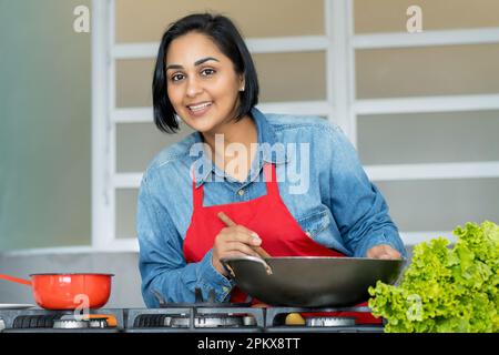 Glückliche lateinamerikanische Frau, die vegetarisches Essen in der Küche zubereitet Stockfoto