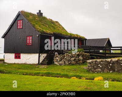 Kirkjubour, Färöer - 2021. Juli: Typisches Färöisches Holzhaus mit roten Fenstern. Nordeuropa Stockfoto