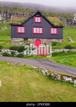 Kirkjubour, Färöer - 2021. Juli: Typisches Färöisches Holzhaus mit roten Fenstern. Nordeuropa Stockfoto