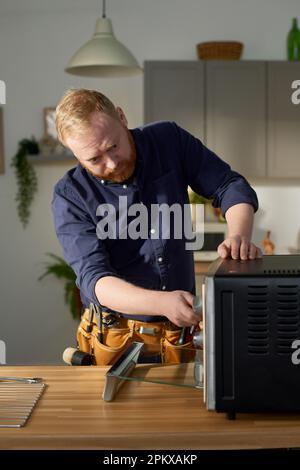 Vertikales Bild eines reifen bärtigen Arbeiters, der sich auf die Reparatur von Geräten zu Hause konzentriert Stockfoto