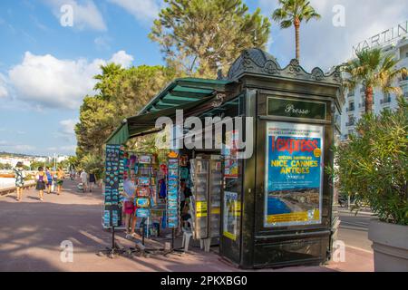 Ein Postkarten- und Souvenirkiosk an der Promenade entlang der Strandpromenade La Croisette in Cannes im Süden Frankreichs mit dem Hotel Mar im weißen Gebäude Stockfoto