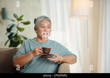 Porträt einer Seniorin, die eine Tasse Tee genießt und wegschaut Stockfoto