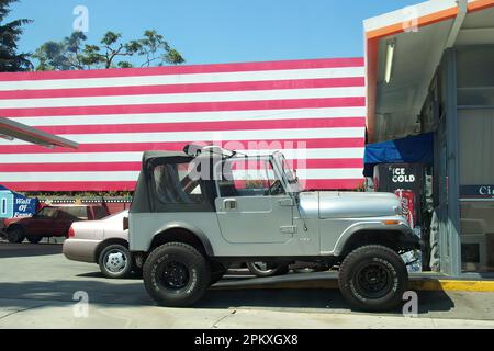 Los Angeles, Kalifornien/USA, 5. August 2004: Grauer Jeep Wrangler parkt an einer Tankstelle in Los Angeles mit einer großen amerikanischen Flagge im Hintergrund. Stockfoto
