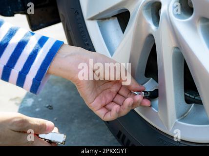 Frau bläst den Reifen auf. Frau, die den Reifendruck überprüft und Luft in den Reifen des Autorads pumpt. Autowartung zur Sicherheit vor der Reise. Stockfoto