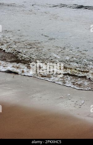 Nahaufnahme der ruhigen Meeresbrise, die bei Sonnenaufgang auf den Strand gespült wird Stockfoto