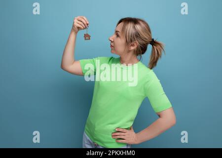 Glückliche, süße blonde Frau in legerem Look mit neuem Schlüsselanhänger auf blauem Hintergrund Stockfoto