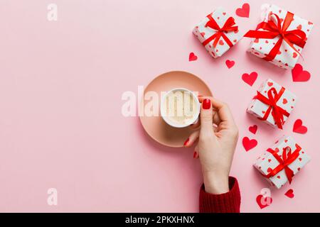 Flache Lage einer herzförmigen Tasse schwarzen Kaffees in den Händen von Frauen auf farbigem Hintergrund mit Kopierbereich Draufsicht. Valentinstag- und Feiertagskonzept. Stockfoto