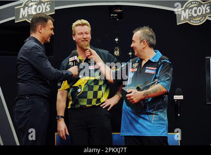 Dateifoto vom 17. Oktober 05/12 von Sky Sports Presenter Dave Clark, der Simon Whitlock interviewt, während Phil Taylor seinen Bart zieht, nachdem Taylor im McCoy's Premier League Darts, PDC Darts Play-Off-Finale, in der O2 Arena, North Greenwich, London, gewonnen hat. Dave Clark ist entschlossen zu zeigen, dass das Leben nicht mit der Diagnose endet, während er weiterhin positiv gegen die Parkinson-Krankheit kämpft. Ausgabedatum: Montag, 10. April 2023. Stockfoto