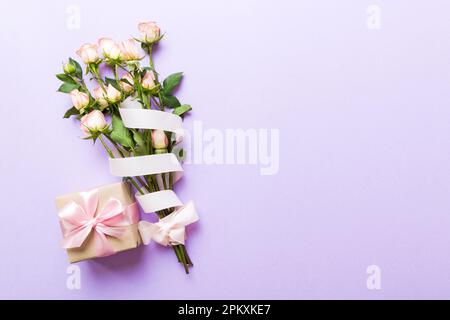 Designkonzept mit rosafarbener Rosenblume und Geschenkbox auf farbigem Tisch, Hintergrundansicht von oben. Frohe Feiertage, Muttertag, Geburtstagskonzept. Romantisches Flat la Stockfoto