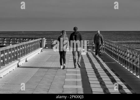 Ein paar junge Männer und Frauen mit einem älteren Mann, die in Schwarz-Weiß an der Promenade des Yachthafens in Denia, Alicante, Spanien und Europa entlang spazieren Stockfoto