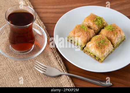 Traditionelles Pistazienbaklava mit türkischem Tee. Ein Teller Baklava auf einem Holztisch Stockfoto