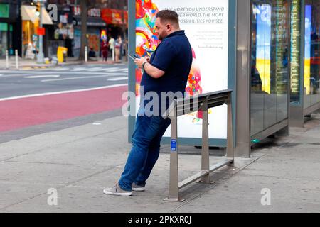 Eine Person, die sich an einer neigenden Bar oder einer neigenden Bank an einer Bushaltestelle in Manhattan in New York City ruht. Feindliche Architektur gegen Sitzen und herumlungern. Stockfoto