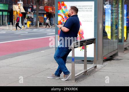 Eine Person, die sich an einer neigenden Bar oder einer neigenden Bank an einer Bushaltestelle in Manhattan in New York City ruht. Feindliche Architektur gegen Sitzen und herumlungern. Stockfoto