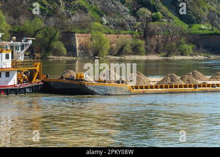 Ein Boot mit flachem Boden, das von einem Schlepper entlang des Flusses geschoben wird, um Kies und Sand zu transportieren. Selektiver Fokus. Stockfoto