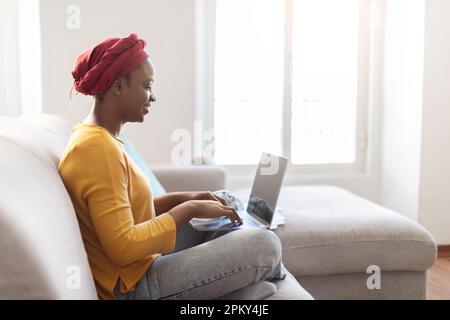 Seitenansicht einer schwarzen Frau, die einen Laptop mit leerem Bildschirm verwendet Stockfoto