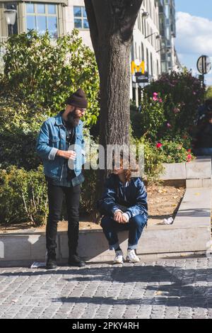 Stilvoller urbaner dialog: Zwei Hipster unterhalten sich in den lebhaften Straßen von Paris, Frankreich Stockfoto