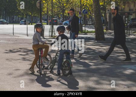 Jungen mit Helmen genießen eine gemeinsame Fahrradtour an einem sonnigen Tag in Paris Stockfoto