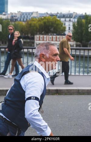 Zeitlose Show: Der 60-jährige Mann in 1940er-Kleidung führt beeindruckende Roller Blade Tricks auf einer Pariser Brücke aus und fasziniert die Zuschauer Stockfoto