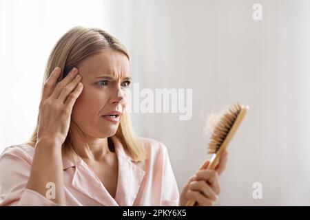 Schockierte, Reife Frau, Die Einen Pinsel Voller Gefallener Haare Ansieht Stockfoto