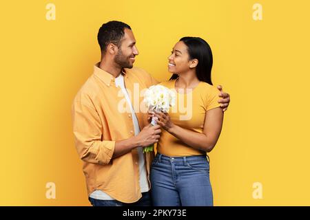 Happy Millennial african american Husband gibt seiner Frau Bouquet und Umarmungen, gratuliert zum Geburtstag Stockfoto