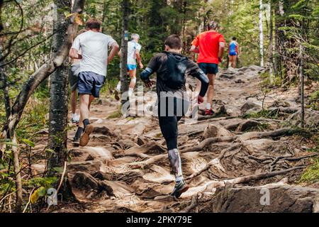 Gruppenläufer Männer und Frauen laufen im Wald ein Marathonrennen auf Steinen und Baumwurzeln Stockfoto