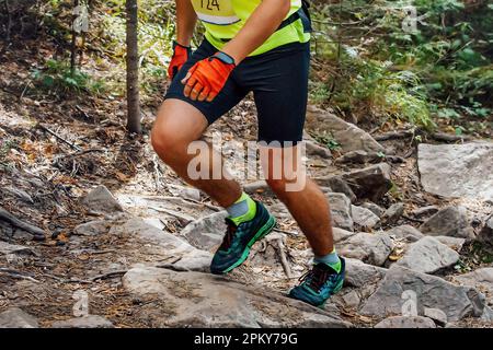 Männlicher Läufer, der Steine bergauf läuft, Marathonrennen im Wald, mit handlosen Handschuhen Stockfoto