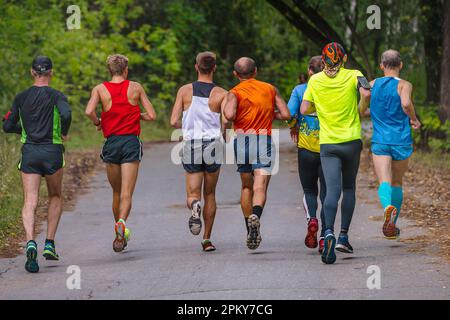 Männliche Läufer in einer kleinen Gruppe veranstalten ein Sportrennen auf der Straße im Park, einen Herbstmarathon, gefallene gelbe Blätter auf dem Boden Stockfoto