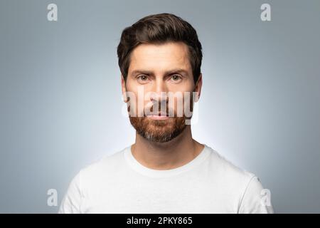Nahaufnahme eines bärtigen, gutaussehenden, weißen Mannes mittleren Alters, der in die Kamera schaut und isoliert vor grauem Hintergrund posiert Stockfoto