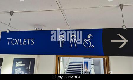 Schild an einem Planetarium mit Wegbeschreibung zu den Toiletten, mit Astronauten innerhalb der Symbole. Stockfoto