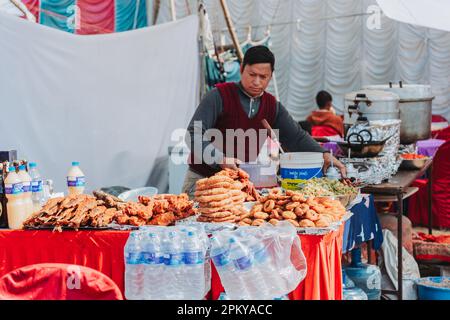 Kathmandu, Nepal - 15. Januar 2023 : Nepalischer Lebensmittelverkäufer, der Lebensmittel wie: Sel Roti, Fried Fish, Samosa, Momo usw. am Imbissstand in Tudikhel arrangiert. Stockfoto