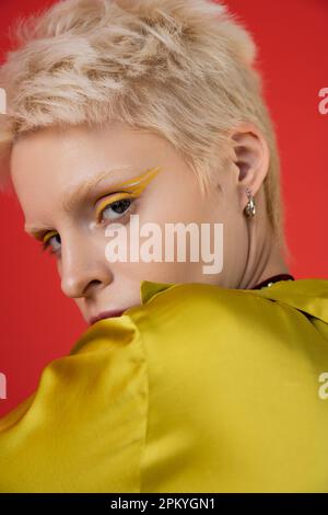 Porträt einer blonden Albino-Frau mit hellem Eyeliner, die auf Karminrosa in die Kamera schaut Stockfoto