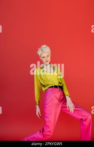 Blonde Frau mit leuchtendem Eyeliner in trendigen Outfits auf karminrosa Hintergrund Stockfoto