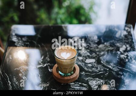 Minimalistischer Kaffee-Latte mit hölzerner Untersetzer auf Marmortisch. Verschwommener Hintergrund Stockfoto