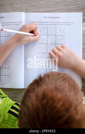 Ein kleiner Junge, der ein Sudoku Workbook für Jugendliche ausfüllt. Das Bild zeigt ein Sudoku-Puzzle (9 x 9 mm), das teilweise vom Jungen vervollständigt wird Stockfoto