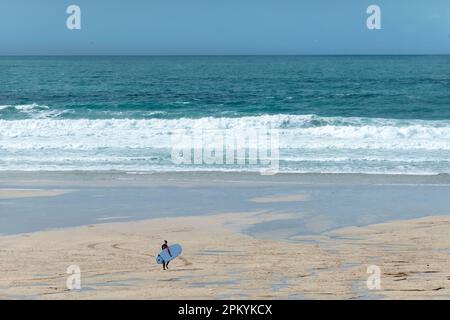Ein einsamer männlicher Surfer geht in Richtung Meer am Fistral Beach, Newquay Cornwall. Er trägt sein Brett, während er den Strand in Richtung der Wellen überquert Stockfoto