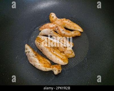 Der selektive Fokus des mit Salz und schwarzem Pfeffer gewürzten Hähnchenfilets wird für die Diätmahlzeit auf der flachen Pfanne gegrillt, Vorderansicht für die Kopien Stockfoto