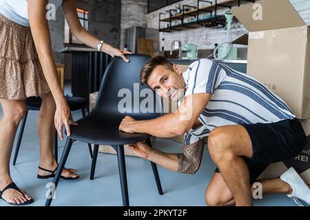 Ein Mann und eine unbekannte verkürzte Frau in lässiger Kleidung, die einen Stuhl zusammenstellt, während sie zusammen in eine neue, moderne Wohnung ziehen Stockfoto