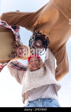 Von unten: Eine fröhliche Gruppe von multirassischen Freunden, die im Sommer lächelnd in die Kamera blicken und die Hände auf den Schultern halten Stockfoto